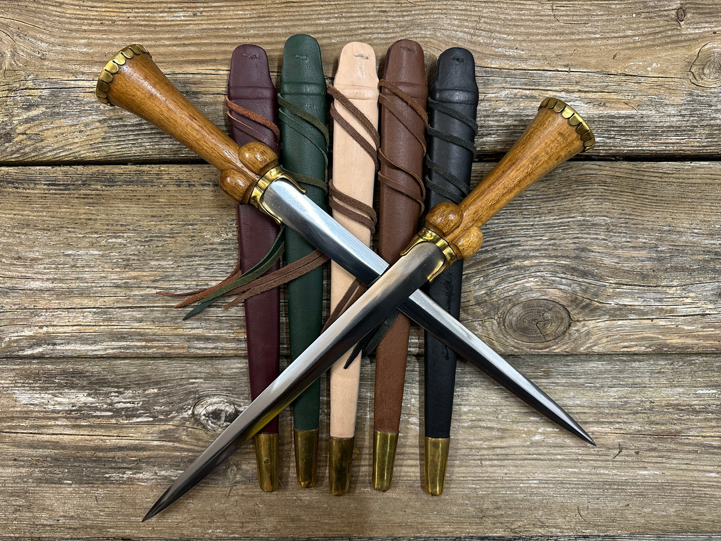 Mid status bollock dagger. Two knives lying on a red, green, natural, brown and black scabbard