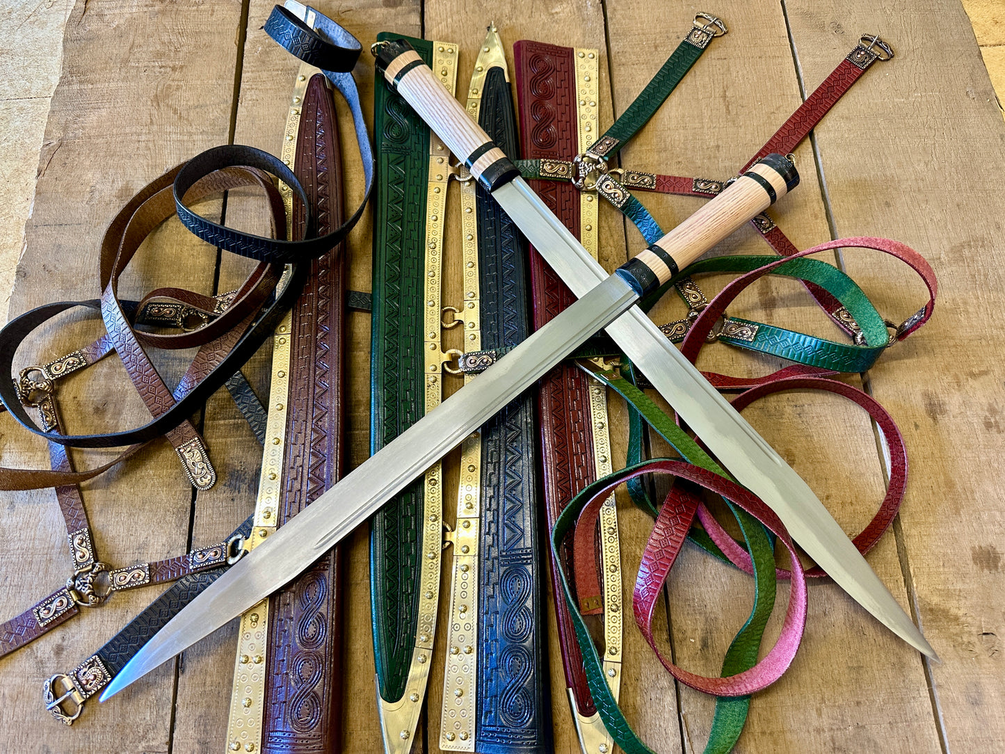 Two crossed sword seax's on a pile of brown, green, black and red scabbards.