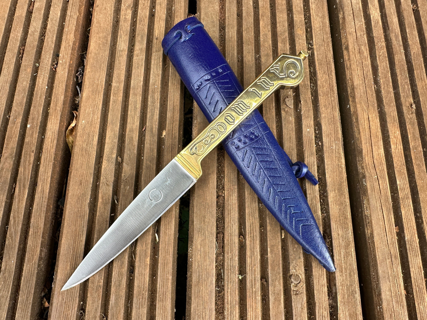 
                  
                    Knife with blue sheath on a wooden surface
                  
                