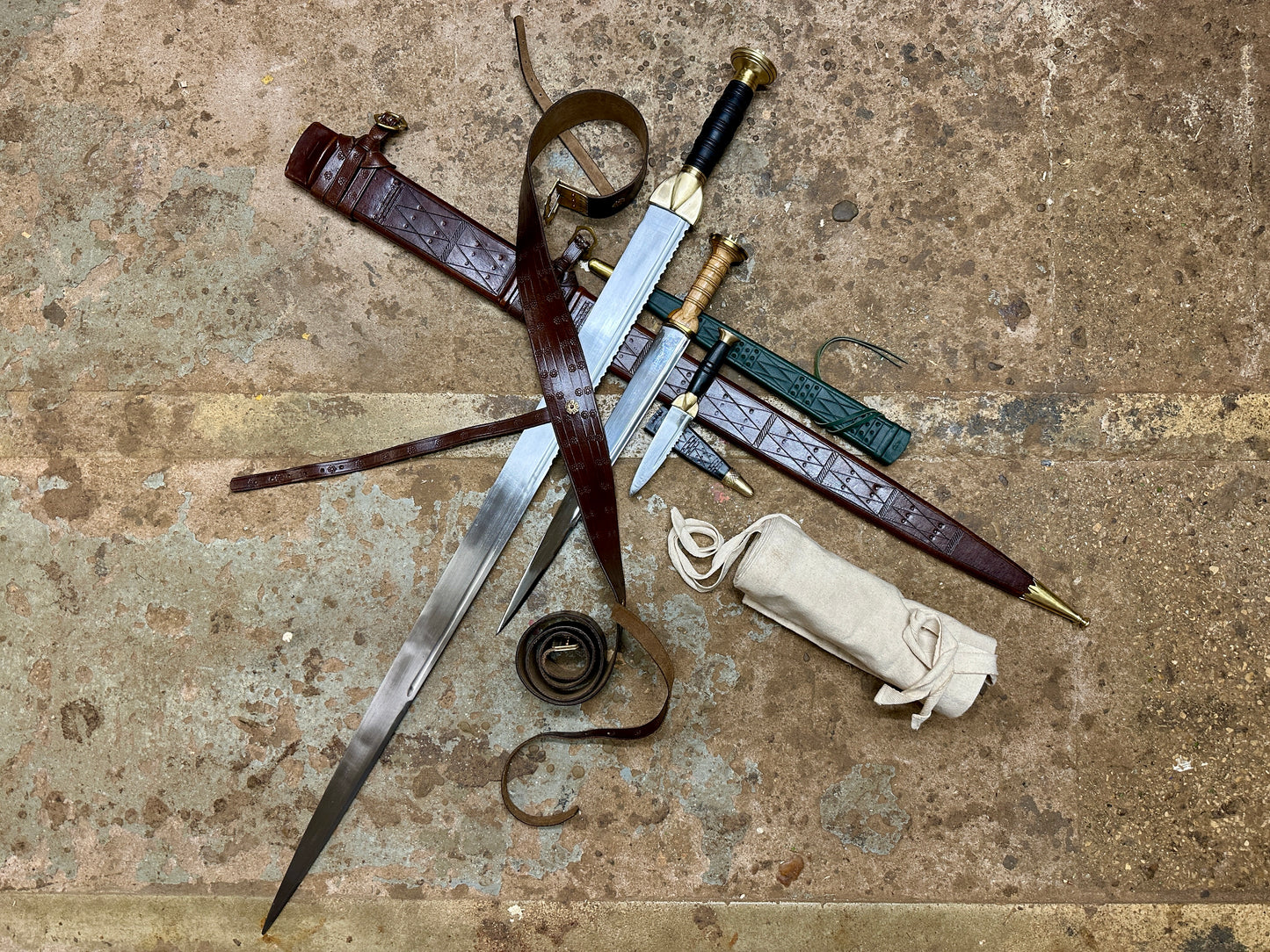 Swirk, Scottish Dirk and Sgian Dhu with their scabbards in a pile with a rolled up sword bag next to them. 