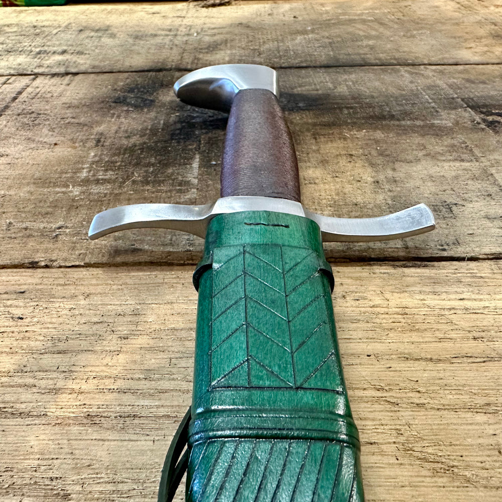 
                  
                    TC108 Wakefield Quillon Dagger. Close up of top half in a green sheath. 
                  
                
