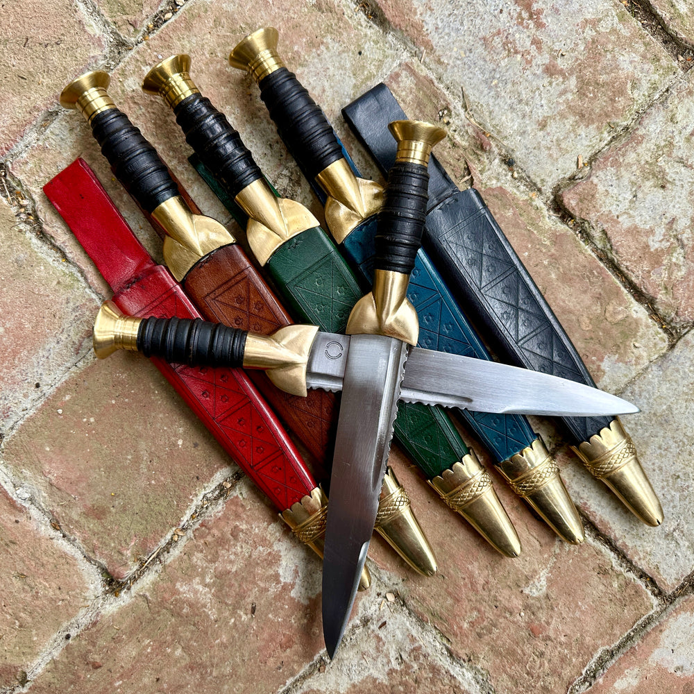 
                  
                    18thC short brass and black wood dirk resting on red, brown, green, blue and black sheathes.
                  
                