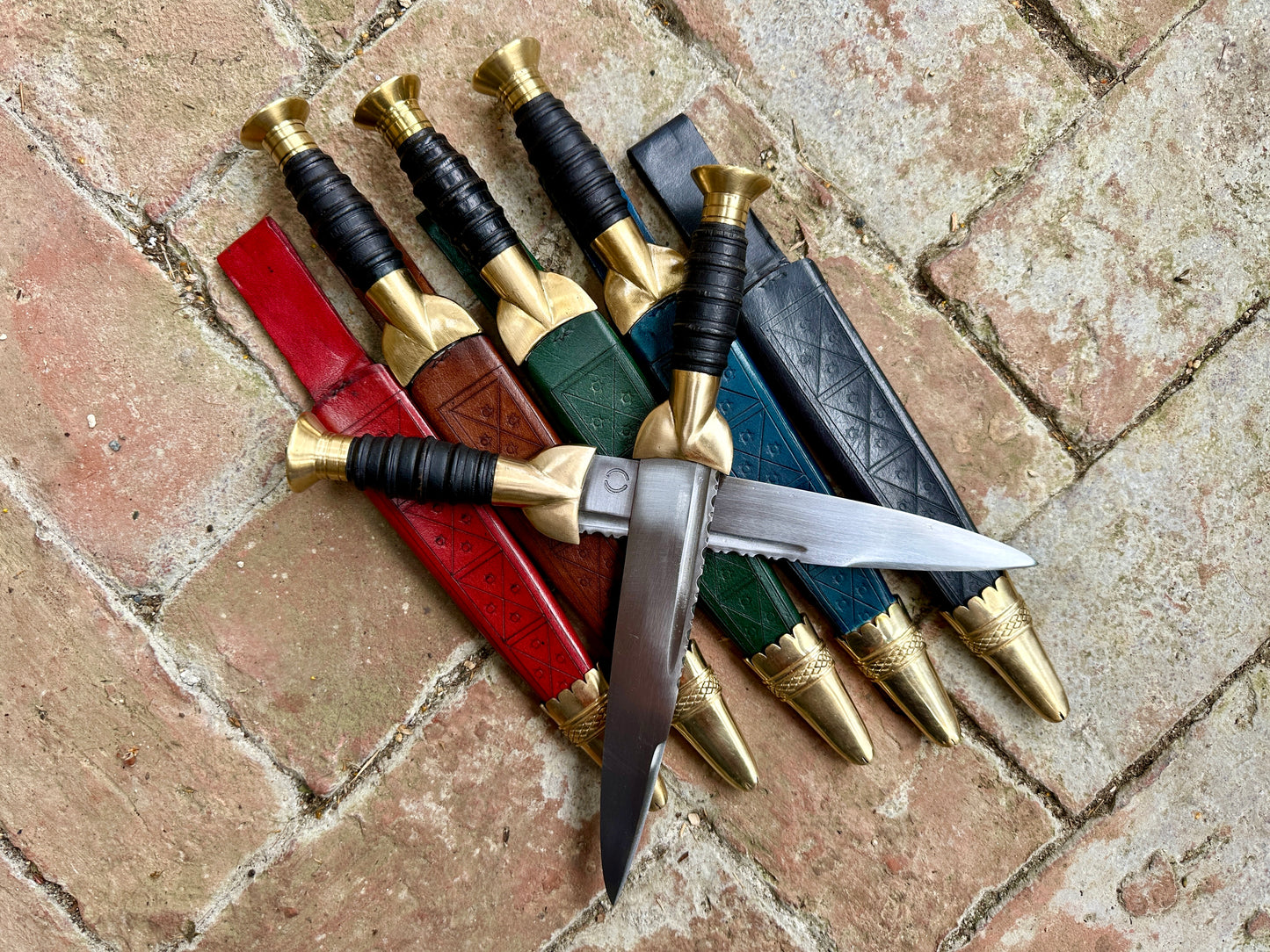 18thC short brass and black wood dirk resting on red, brown, green, blue and black sheathes.