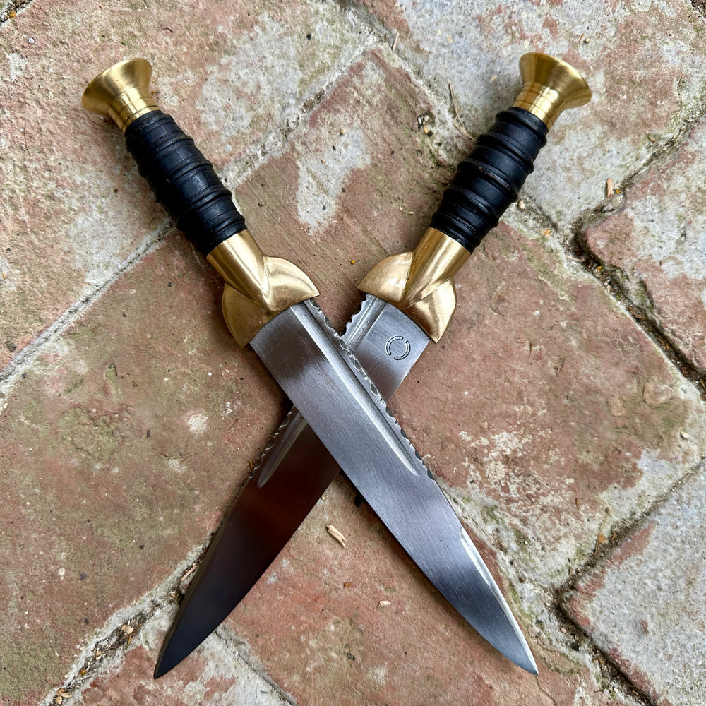 
                  
                    18thC short brass and black wood dirk. Two knives crossed. 
                  
                