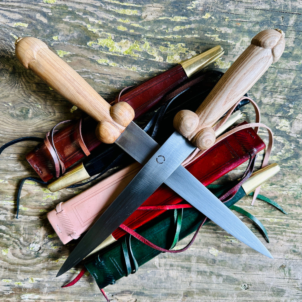 
                  
                    Two rude bollock daggers on a bed of scabbards in red, black, natural, brown and green
                  
                