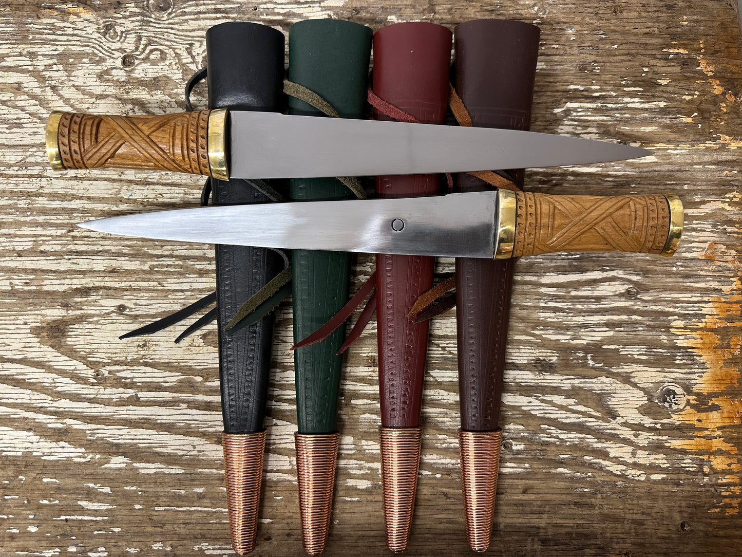 2 short irish skean resting on a black, green, red and brown scabbard. 