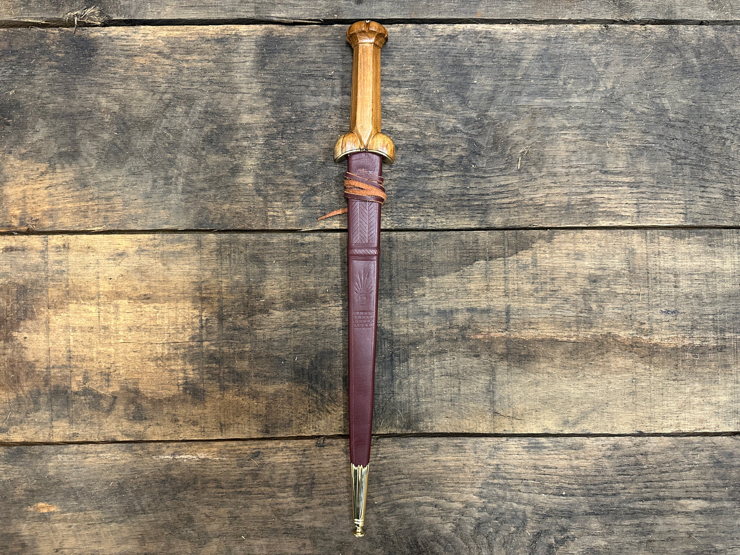 
                  
                    A Mary Rose Bollock Dagger in a red sheath on a wooden background. 
                  
                