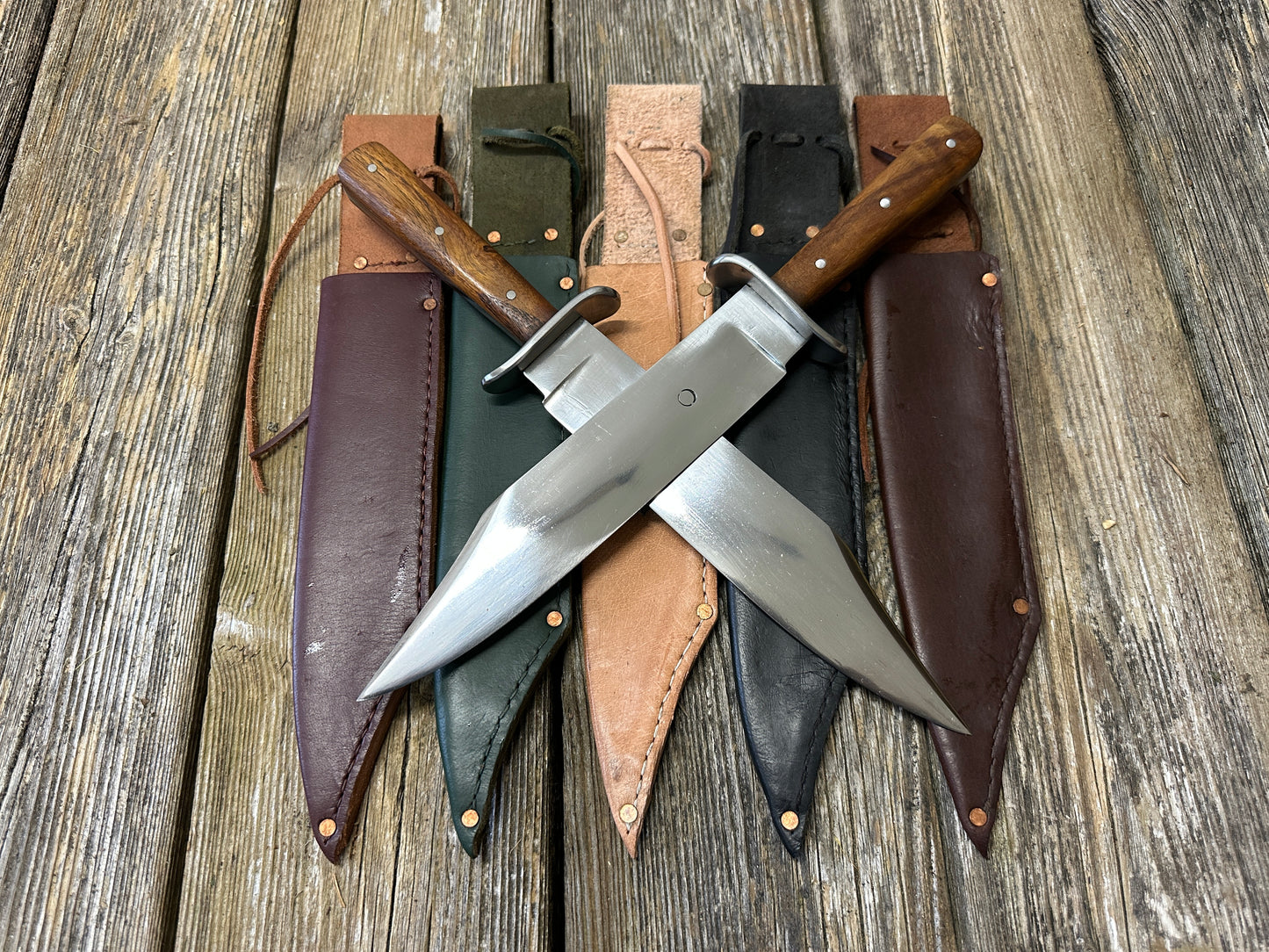 Two Bowie knives crossed on red, green, natural, black and brown scabbards