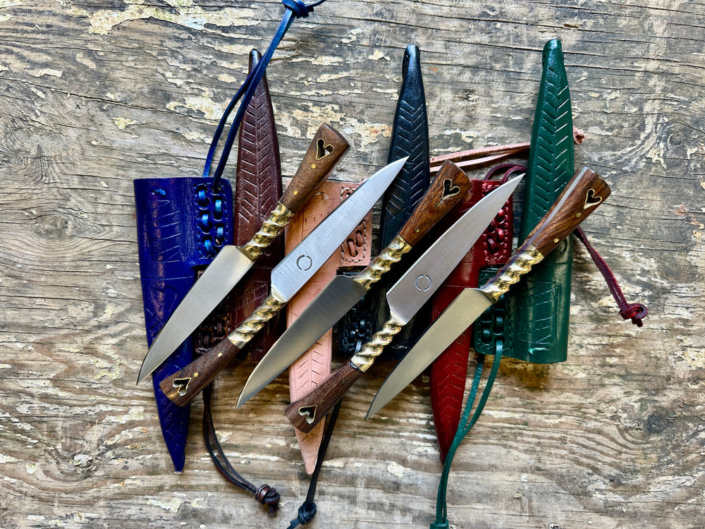 5 heart eating knives on a pile of blue, brown, natural, black, red and green sheathes.