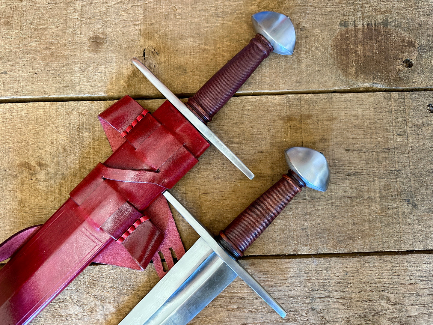 
                  
                    Two Viking Norman Brazil Nut Swords next to each other, one in a red scabbard
                  
                