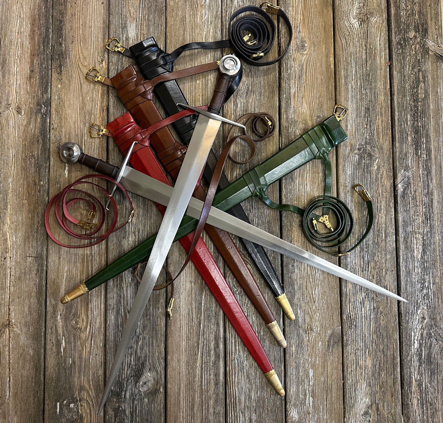 Two Castillon swords resting on red, brown, black and green scabbards with curled belts all around. 