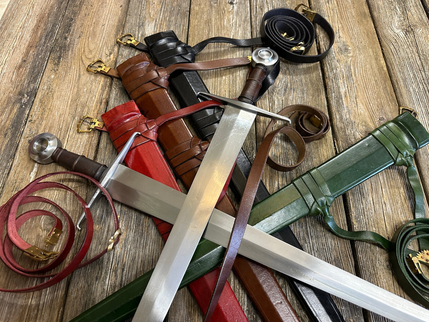 Two Castillon swords resting on red, brown, black and green scabbards with curled belts all around. Zoomed in 